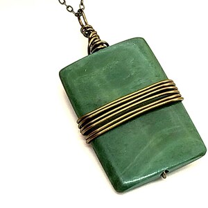 May include: A rectangular green stone pendant suspended from a thin bronze-toned metal chain. The pendant is secured with coiled bronze wire wrapping around its center and features a small metal loop at the top for attachment to the chain.