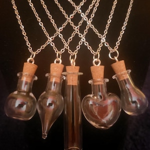 Può includere: Cinque collane con bottiglie di vetro e tappi di sughero. Le bottiglie sono di forme diverse, tra cui rotonda, a goccia, a forma di cuore e cilindrica. Le collane sono catene argentate.
