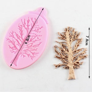 Puede incluir: Un molde de silicona rosa en forma ovalada con un diseño de árbol, de 9,8 cm. Junto a él, un objeto con forma de árbol de color bronce, de 7,8 cm de altura. El diseño del árbol presenta intrincadas ramas, adecuado para manualidades o repostería.