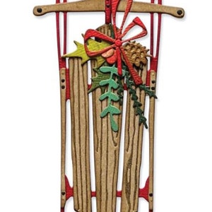 Può includere: Una slitta decorativa in legno con dettagli rossi e una composizione festosa. La slitta presenta un design in legno marrone con pattini rossi e una parte superiore argentata. È adornata con un fiocco rosso, foglie verdi e una pigna, creando un tema festivo.