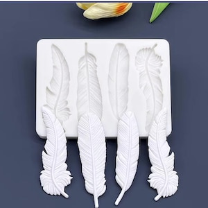 Pode incluir: Forma de silicone branca com seis formas de penas. A forma é projetada para criar toppers de bolo decorativos ou outras decorações comestíveis.