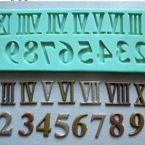 May include: A set of Roman numeral and Arabic numeral charms in gold, silver, and bronze. The charms are arranged in two rows on a blue surface. The top row features Roman numerals I through XII, and the bottom row features Arabic numerals 1 through 10.