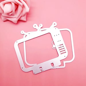 May include: A set of three silver metal die-cut shapes of a vintage television. The shapes are layered on top of each other.