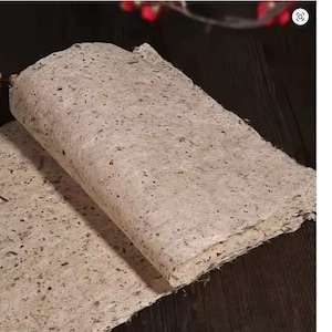 May include: Two sheets of handmade paper with a speckled, textured surface. The paper has a natural, off-white color with flecks of brown and black throughout. The sheets are slightly rolled, revealing the layered edges. Ideal for crafts and stationery.