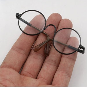 May include: A pair of black round glasses with brown plastic arms. The glasses are held in a hand.