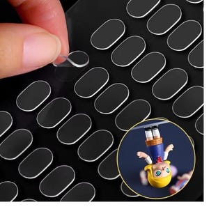 May include: A close-up of a person peeling a clear sticker from a sheet of black, oval-shaped stickers with white borders. A small, circular inset shows a cartoon figure.