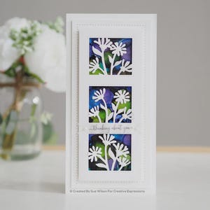May include: A white card with three rectangular cutouts, each showcasing a floral design. The cutouts reveal a colorful background of blue, purple, and green. The text "thinking about you" is written across the card.
