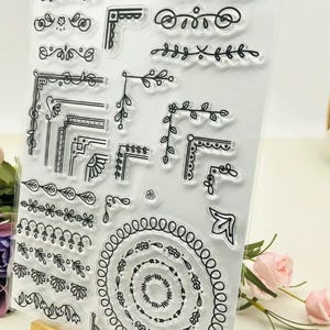 May include: Clear sheet of transparent stamps with various black line designs. The designs include borders, corners, swirls, and floral patterns.