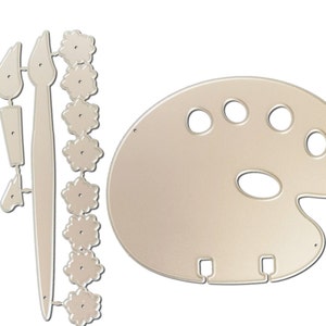 May include: A die-cut set of art-themed shapes in a light beige color. The set includes a painter's palette with oval and round paint wells, two paintbrushes, and a string of flower-shaped embellishments. The shapes are designed for crafting and art projects.