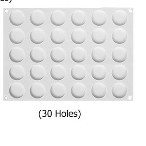 Peut inclure: Un moule de cuisson en silicone blanc avec 30 empreintes circulaires. Le moule est rectangulaire avec des coins arrondis et de petits trous dans chaque coin. Le texte "(30 Holes)" est imprimé en dessous.