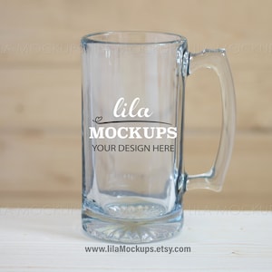 May include: A clear glass beer mug with a handle. The mug has the text "lila MOCKUPS YOUR DESIGN HERE" printed on the side.