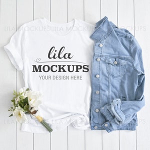 May include: White t-shirt with the text "lila MOCKUPS YOUR DESIGN HERE" on a white wood background with a blue denim jacket and a bouquet of white flowers.