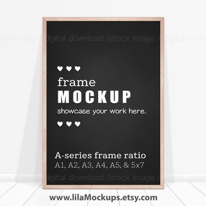 May include: A black frame mockup with a white wooden frame. The frame is on a white wood floor and a white wall. The text on the frame reads "frame MOCKUP showcase your work here." and "A-series frame ratio A1, A2, A3, A4, A5, & 5x7".