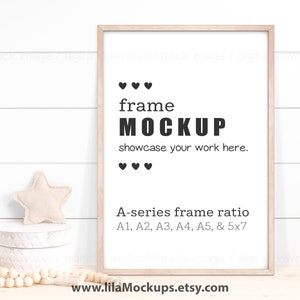 May include: A light wood frame mockup with the text "frame MOCKUP" and "showcase your work here." The frame is on a white wood background with a small star-shaped pillow and a white decorative box with wooden beads in front of it. The text "A-series frame ratio A1, A2, A3, A4, A5, & 5x7" is below the frame.