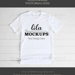 K&ouml;nnte beinhalten: Wei&szlig;es T-Shirt-Mockup mit dem Text "lila MOCKUPS" und "Your Design Here" auf wei&szlig;em Holz Hintergrund.