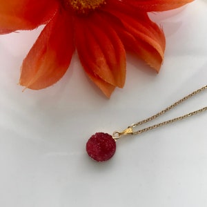 May include: A gold chain necklace with a red crystal pendant. The pendant is round and has a rough, textured surface.