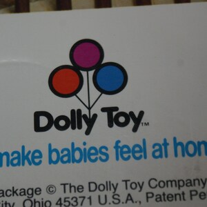 May include: White background with the Dolly Toy logo, featuring three connected circles in red, purple, and blue. Below the logo, the text reads "We make babies feel at home."