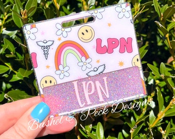 May include: A pink and white glitter badge holder with a rainbow, smiley faces, and the text "LPN".