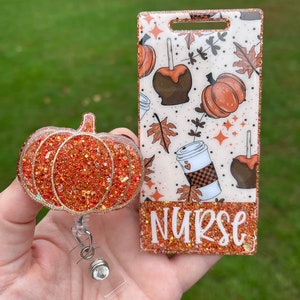 Puede incluir: Un charm de calabaza de purpurina naranja brillante con un soporte de credencial retráctil transparente y un soporte de credencial de purpurina blanca y naranja con un diseño de otoño y la palabra "NURSE" en purpurina blanca.