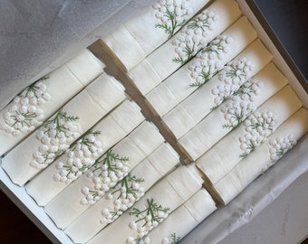 May include: A set of 12 white linen napkins with embroidered green stems and white flower clusters.