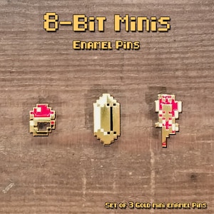 May include: Set of three gold mini enamel pins with a pixelated design. The pins include a gold ring with a red top, a gold shield, and a red and white flower. The text "8-Bit Minis" and "Enamel Pins" are displayed.