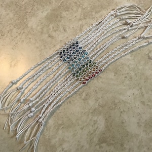 May include: A set of 10 rainbow beaded friendship bracelets with white string. The bracelets are tied together at the ends.