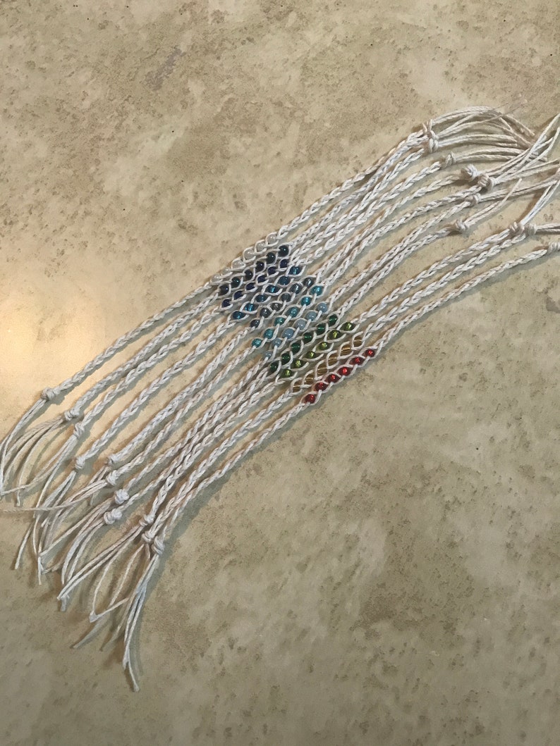 May include: A set of 10 rainbow beaded friendship bracelets with white string. The bracelets are tied together at the ends.