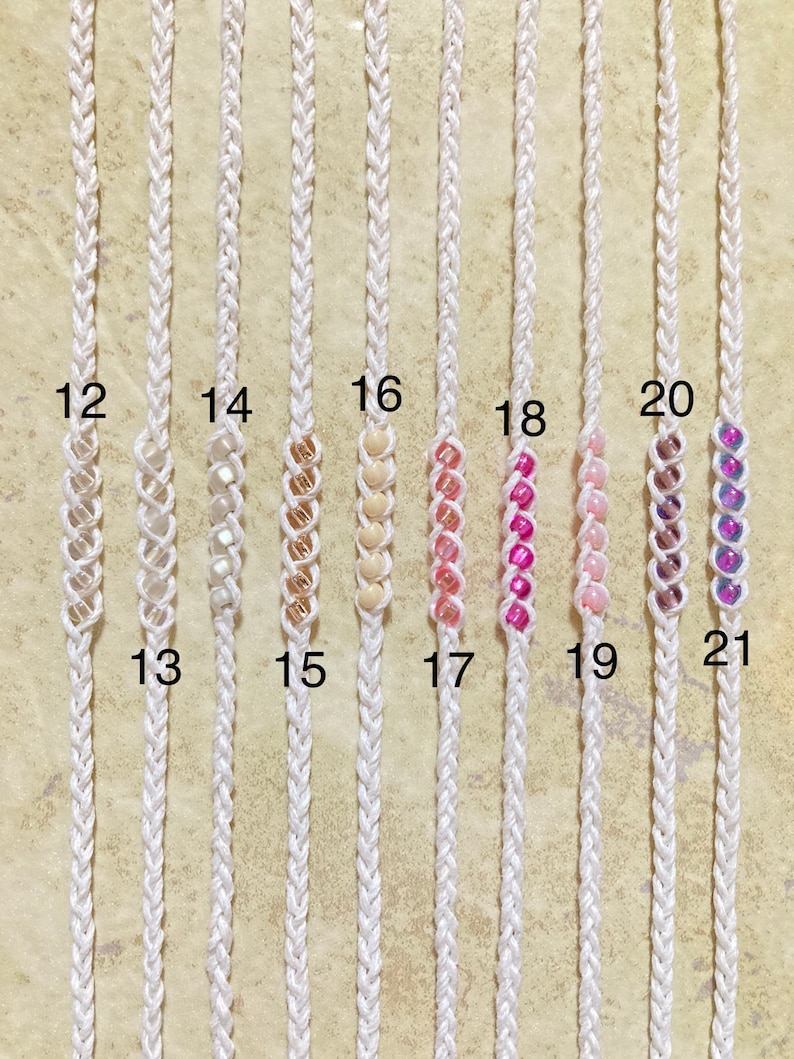 May include: A close-up of ten white macrame cords with beads. The cords are numbered 12 through 21. The beads are different colors, including white, gold, pink, and purple.