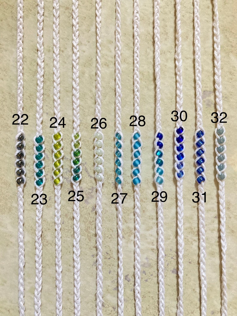 May include: Ten white cords with different colored beads strung on them. The cords are numbered 22 through 32. The beads are in various shades of blue, green, and white.