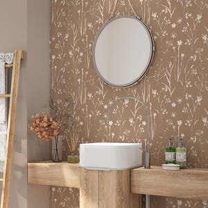 May include: A bathroom featuring brown floral wallpaper, a wooden vanity unit, and a white rectangular sink. A round mirror hangs above the sink. A wooden towel rack is on the left. The tap and soap dispensers are silver.