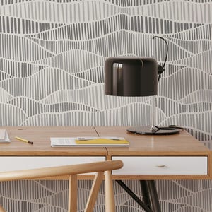 May include: A black desk lamp with a rounded shade sits on a wooden desk. The desk has a white drawer and a yellow notepad. The background features a gray and white abstract pattern resembling mountain ranges.