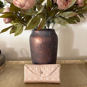 May include: A rectangular fabric pouch featuring a light peach and white geometric floral pattern. The pouch has a triangular flap secured with a single silver-toned metal snap button centered on the front, creating a compact envelope-style design.