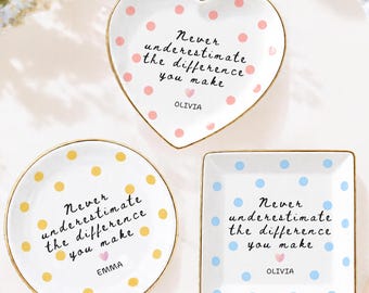 May include: Three ceramic trinket dishes with gold-toned rims. One heart-shaped dish with pink polka dots, one round dish with yellow polka dots, and one square dish with blue polka dots. Each features the text Never underestimate the difference you make.