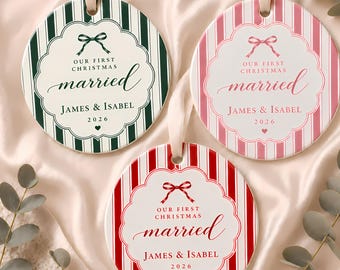 May include: Three round ceramic ornaments with satin ribbons. Each features vertical stripes in dark green, pink, or red, a central scalloped frame, a bow graphic, and the text "OUR FIRST CHRISTMAS married JAMES & ISABEL 2026" with a small heart.