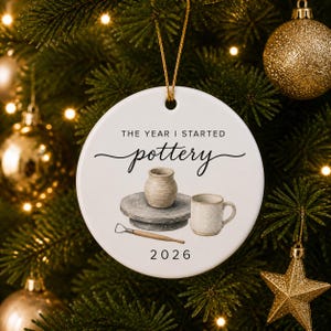 White ceramic pottery ornament hanging from a gold string on a warmly lit Christmas tree.
