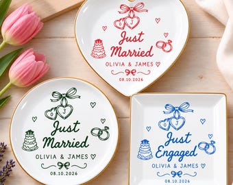 May include: Three white ceramic trinket dishes with gold rims. One heart-shaped dish in red features 'Just Married', 'OLIVIA & JAMES', and '08.10.2026'. A round green dish and a square blue dish both feature 'Just Married' or 'Just Engaged'.