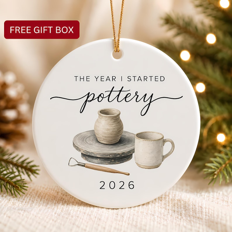 The Year I Started Pottery Ornament shown as a round white ceramic keepsake with watercolor pottery wheel, vase, mug, clay tool, gold cord, year 2026 and free gift box.