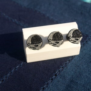 May include: Three silver and black cufflinks with a geometric design. The cufflinks are displayed on a white surface.