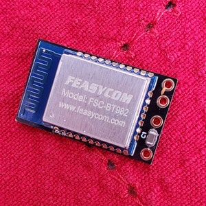 May include: A small blue circuit board with a silver chip that says "FEASYCOM Model: FSC-BT982 www.feasycom.com".