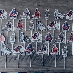 Puede incluir: Una colecci&oacute;n de veintis&eacute;is adornos para cupcakes, cada uno con un recorte fotogr&aacute;fico &uacute;nico de una persona y el texto impreso Happy 70th. Cada recorte est&aacute; montado sobre un palillo blanco fino para insertar en alimentos.