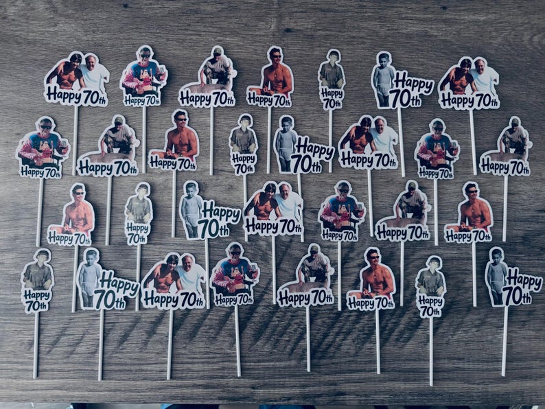 Puede incluir: Una colecci&oacute;n de veintis&eacute;is adornos para cupcakes, cada uno con un recorte fotogr&aacute;fico &uacute;nico de una persona y el texto impreso Happy 70th. Cada recorte est&aacute; montado sobre un palillo blanco fino para insertar en alimentos.