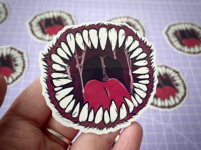 May include: A sticker of a large, open mouth with sharp teeth and a red tongue. The mouth is surrounded by a red, furry border.