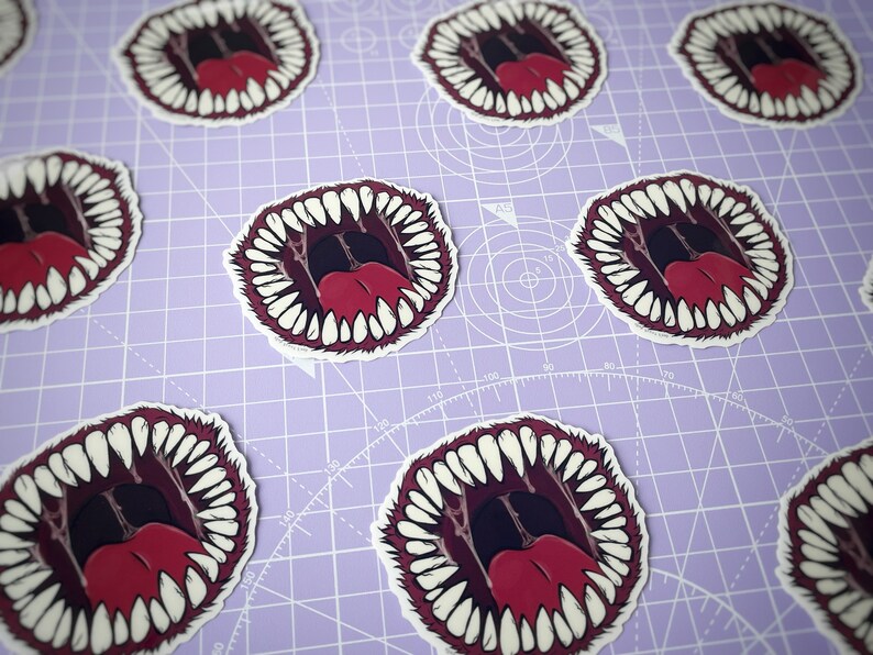 May include: A set of stickers featuring a cartoon mouth with sharp teeth and a red tongue. The stickers are printed on white paper and have a glossy finish.