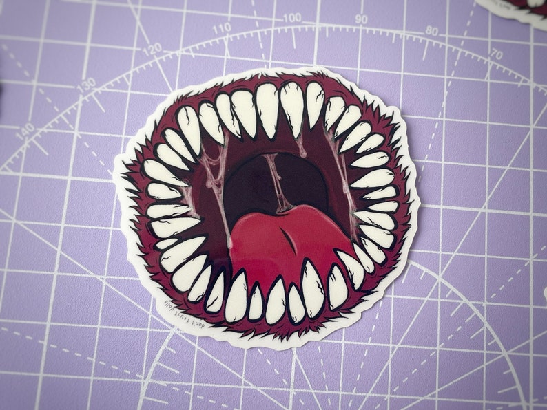 May include: A sticker of a large, open mouth with sharp, white teeth and a red tongue. The mouth is surrounded by a red, furry border.