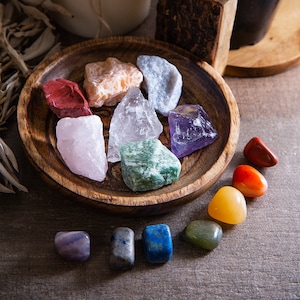 May include: A wooden bowl filled with seven different colored crystals, including red, orange, yellow, green, blue, indigo, and violet. The crystals are arranged in a circle around the bowl, with a smaller set of crystals in a row below the bowl.