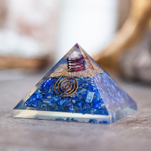 May include: A blue crystal pyramid with a copper wire spiral inside. The pyramid is filled with small blue crystals and has a clear base.
