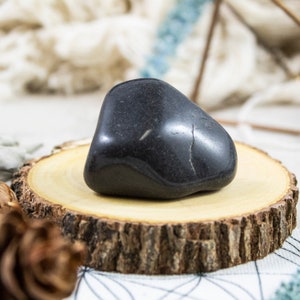 May include: A smooth, black obsidian stone resting on a wooden slice. The stone has a natural, polished finish and is a popular choice for crystal healing.