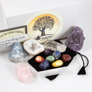May include: A set of seven chakra healing stones in a velvet pouch, with a selenite charging wand, a clear quartz crystal, a blue calcite crystal, a rose quartz crystal, and an amethyst crystal. The set is packaged in a white box with a certificate of authenticity.