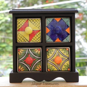 May include: A black wooden box with four small drawers. Each drawer has a colorful ceramic front with a different geometric pattern and a knob. The box is labeled "Jaipur Treasures".
