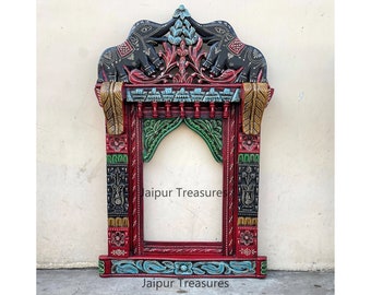 Puede incluir: Un marco de madera colorido con dos elefantes tallados en la parte superior. El marco está pintado en tonos de rojo, verde, negro y dorado. El marco tiene un diseño de arco decorativo y es perfecto para un espejo o una imagen. El texto "Jaipur Treasures" está escrito en la parte inferior del marco.